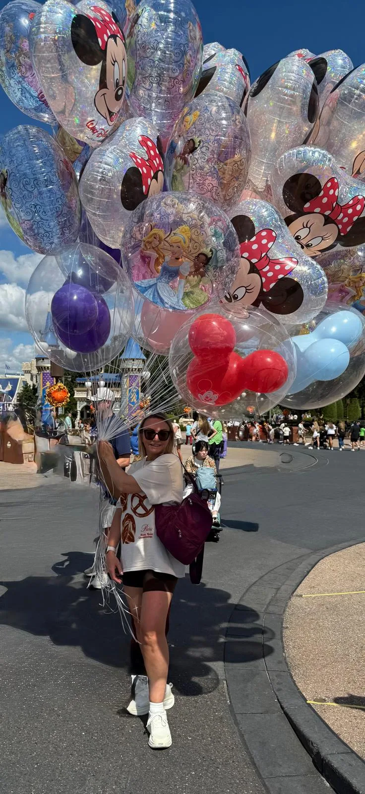 Sam carrying a large bunch of Mickey and Minnie Mouse balloons at a Disney park in Florida