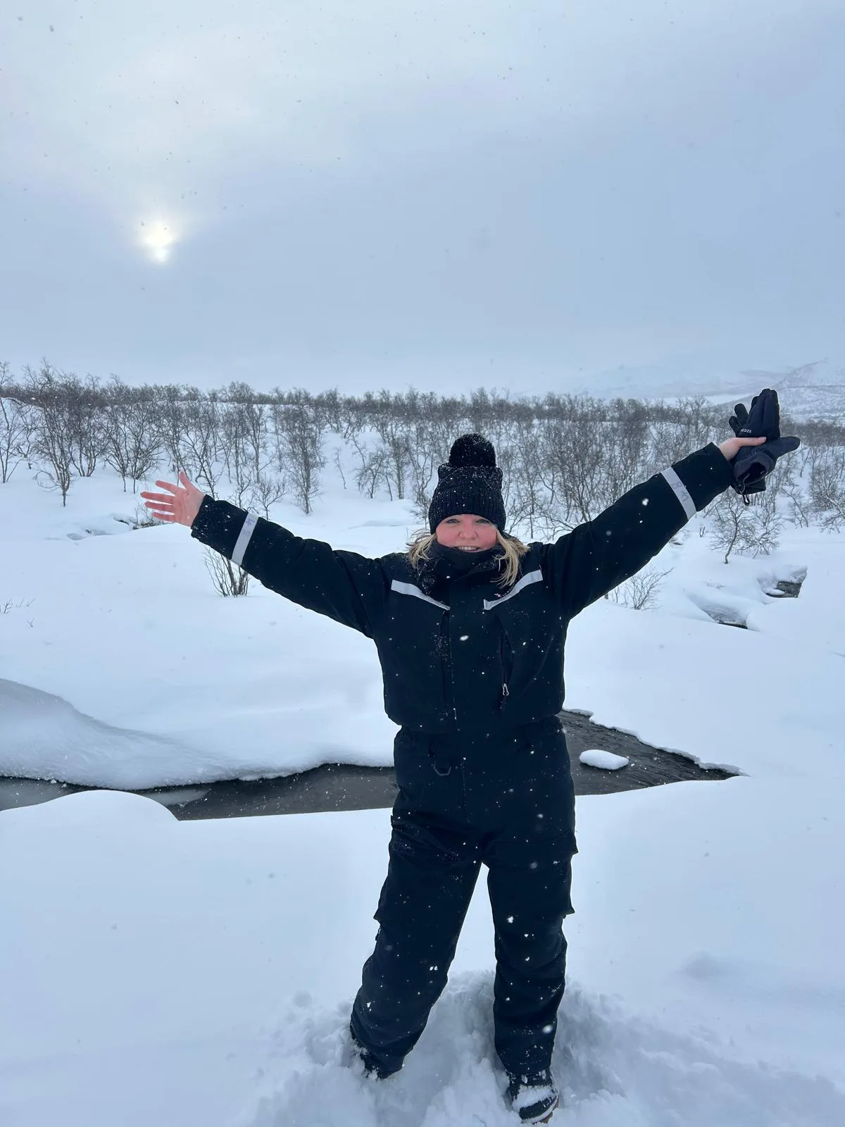 Sam standing in deep snow in a full snowsuit with her arms outstretched