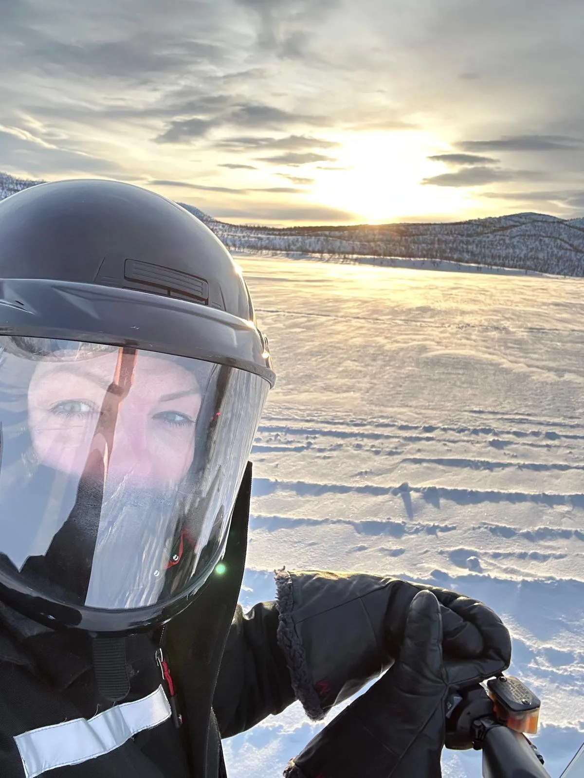Sam in a snowmobile helmet on a frozen lake in Finnish Lapland, low sun behind her